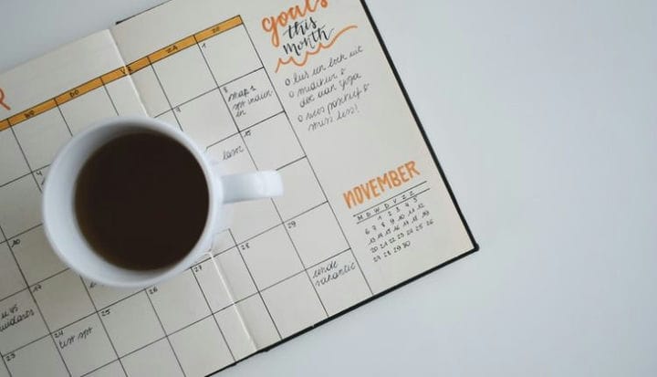white ceramic mug with coffee on top of a planner