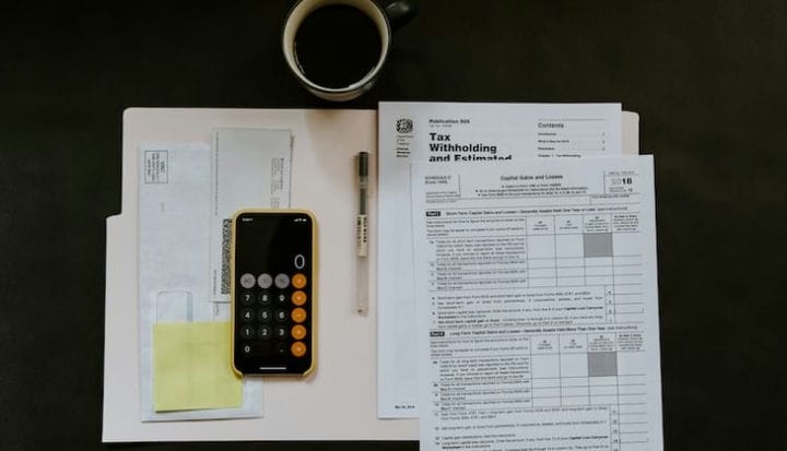black Android smartphone near ballpoint pen, tax withholding certificate on top of white folder